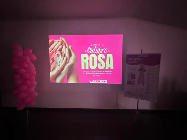 Projeção da campanha Outubro Rosa sobre prevenção e diagnóstico precoce do câncer de mama, com banner informativo da Lorenzi.